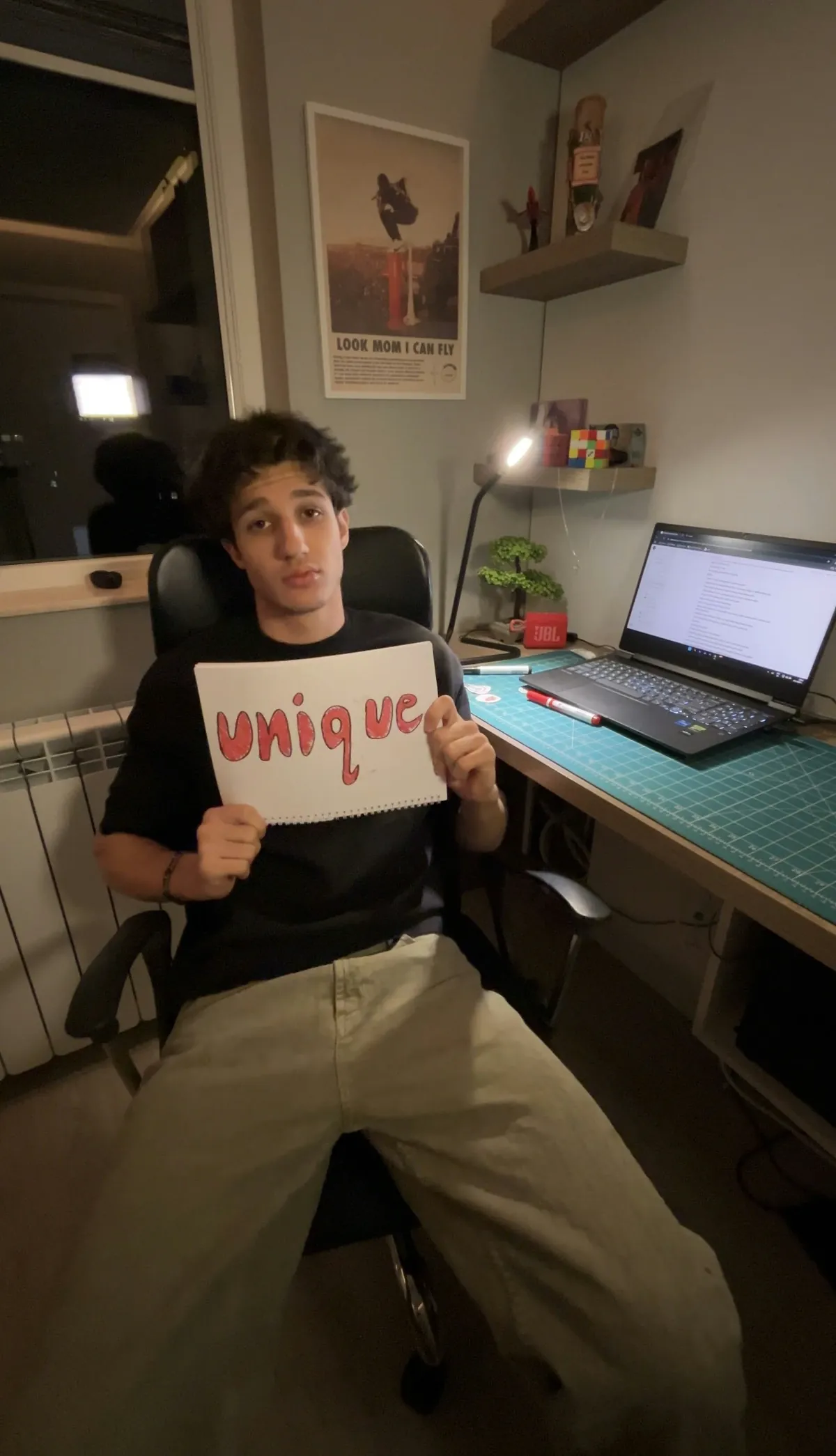 Emil at his desk holding a sign that reads unique